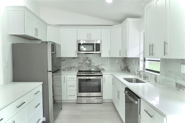 kitchen featuring stainless steel appliances, lofted ceiling, white cabinetry, and backsplash