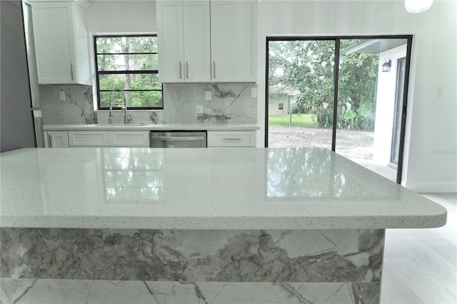 kitchen featuring stainless steel dishwasher, white cabinetry, sink, and light stone counters