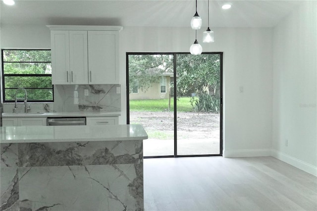 kitchen featuring light stone counters, white cabinets, light hardwood / wood-style flooring, decorative light fixtures, and sink