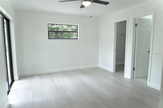 unfurnished bedroom with light hardwood / wood-style flooring, a closet, ceiling fan, and a walk in closet