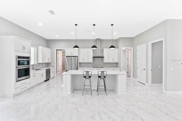 kitchen with pendant lighting, white cabinets, a kitchen island, wall chimney range hood, and appliances with stainless steel finishes