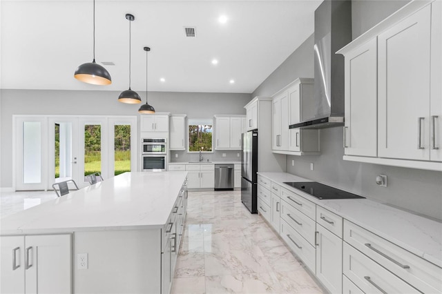 kitchen with a large island, decorative light fixtures, wall chimney exhaust hood, white cabinetry, and stainless steel appliances