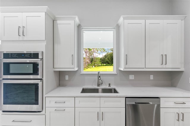 kitchen with light stone countertops, stainless steel appliances, sink, and white cabinetry