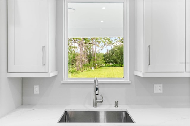 kitchen with white cabinetry, light stone countertops, and sink