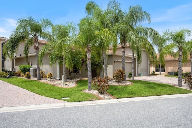 view of front facade featuring stucco siding, decorative driveway, a front yard, central AC, and a garage