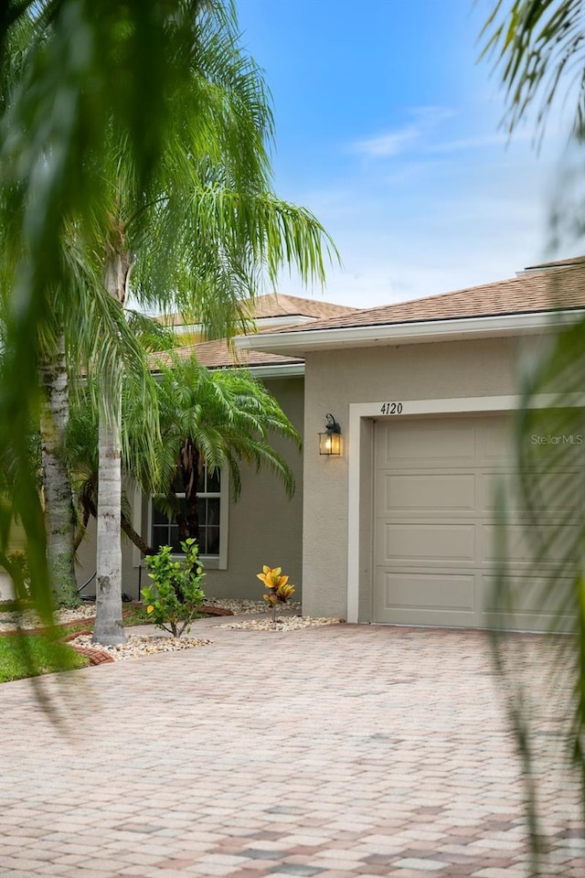 view of exterior entry with stucco siding, an attached garage, and decorative driveway