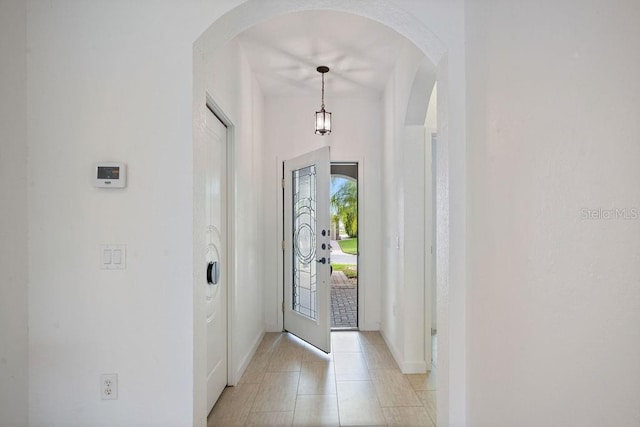 foyer featuring baseboards, arched walkways, and light tile patterned floors