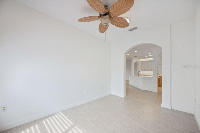 spare room with a sink, baseboards, visible vents, arched walkways, and ceiling fan