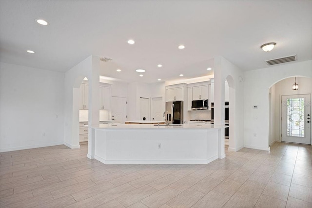 kitchen with light countertops, a large island, stainless steel appliances, visible vents, and arched walkways