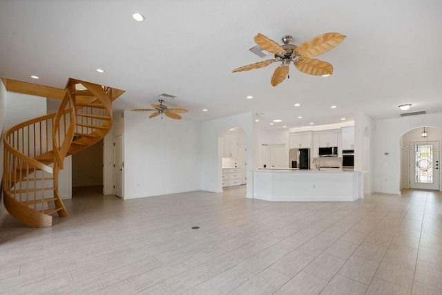 unfurnished living room featuring arched walkways, ceiling fan, and stairway