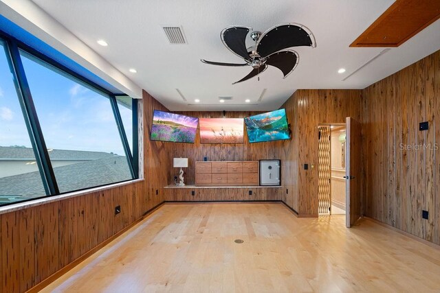 unfurnished room with ceiling fan, light wood-type flooring, and wood walls