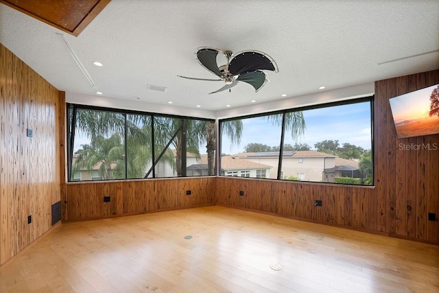 spare room with light wood-type flooring, wood walls, ceiling fan, and a textured ceiling