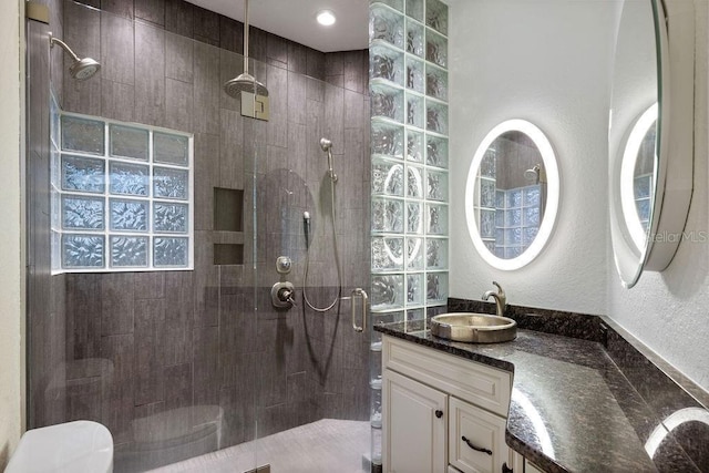 bathroom with toilet, vanity, a textured wall, and a walk in shower