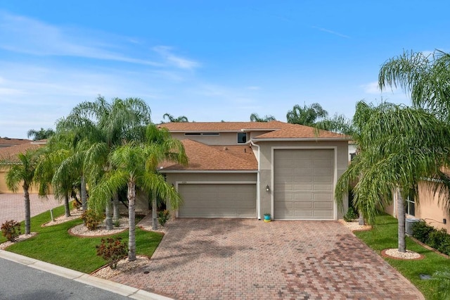 view of front of home with stucco siding, an attached garage, a front lawn, and decorative driveway