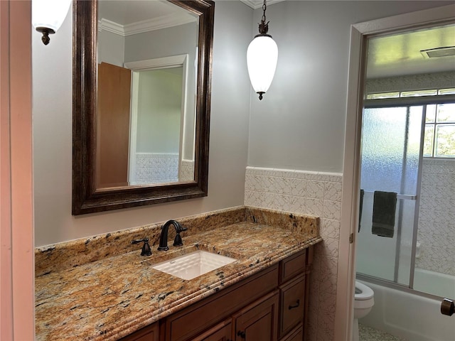 bathroom featuring tile walls, toilet, ornamental molding, combined bath / shower with glass door, and vanity