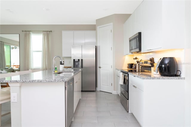 kitchen with appliances with stainless steel finishes, white cabinetry, a kitchen bar, a kitchen island with sink, and sink