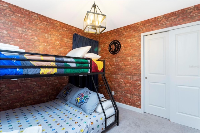 carpeted bedroom with an inviting chandelier, a closet, and brick wall