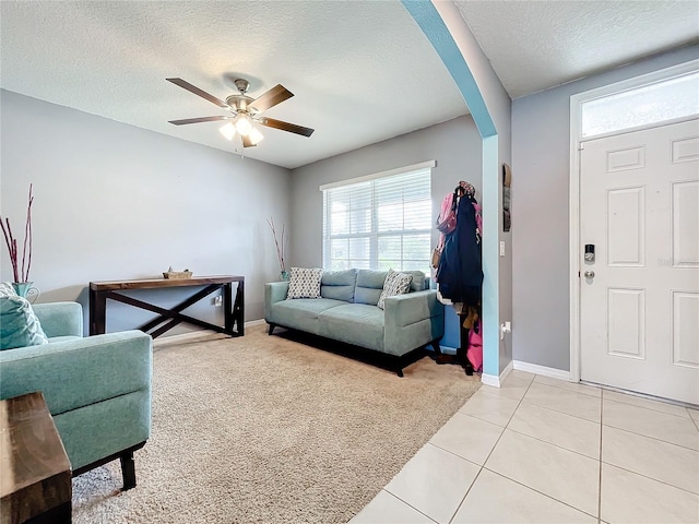 living room with ceiling fan, a textured ceiling, and light tile patterned flooring