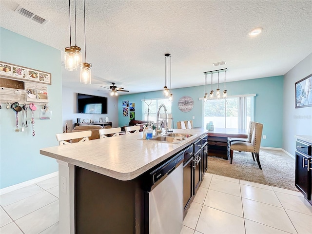 kitchen featuring ceiling fan, stainless steel dishwasher, a textured ceiling, decorative light fixtures, and a kitchen island with sink