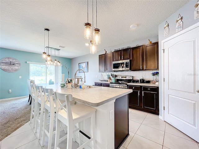 kitchen with appliances with stainless steel finishes, a kitchen breakfast bar, a textured ceiling, a kitchen island with sink, and a notable chandelier