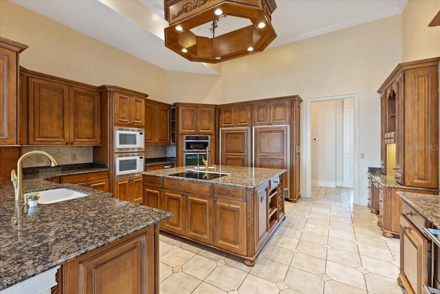 kitchen featuring an island with sink, dark stone counters, sink, and a high ceiling