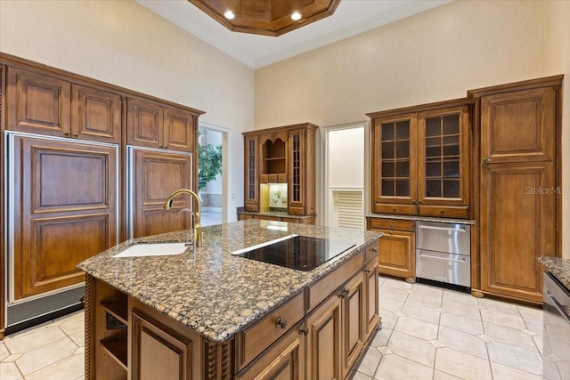 kitchen featuring a high ceiling, a tray ceiling, black electric stovetop, a kitchen island with sink, and sink