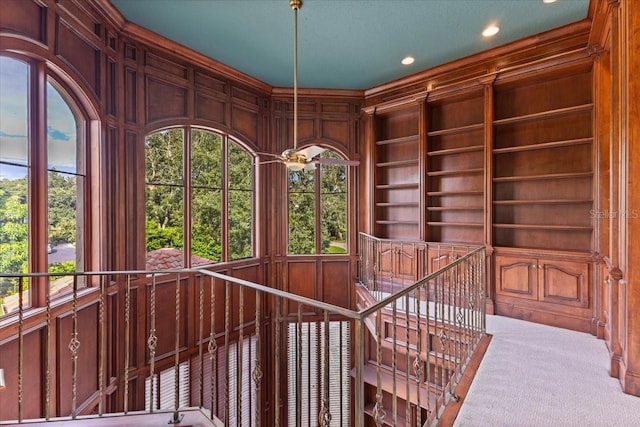 interior space featuring built in shelves, wooden walls, carpet flooring, and ceiling fan