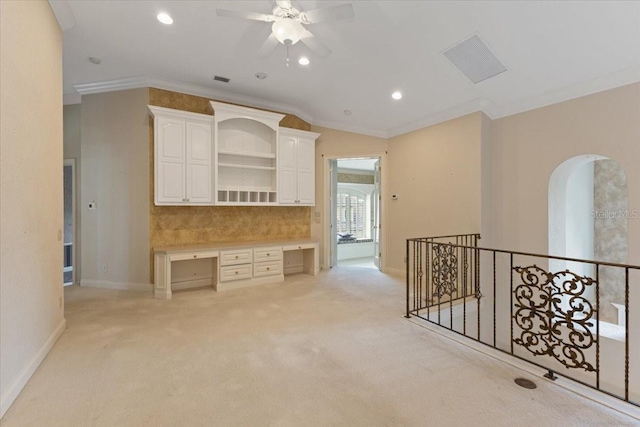 interior space featuring built in desk, crown molding, ceiling fan, and light carpet