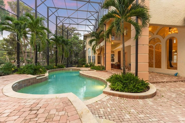 pool at dusk featuring a lanai and a patio