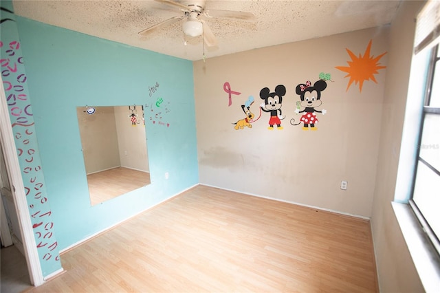 spare room featuring ceiling fan, a healthy amount of sunlight, light wood-type flooring, and a textured ceiling