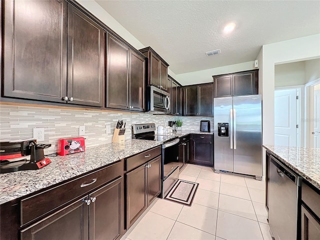 kitchen featuring dark brown cabinets, light stone counters, a textured ceiling, decorative backsplash, and appliances with stainless steel finishes