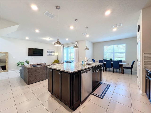 kitchen with hanging light fixtures, light stone countertops, a center island with sink, stainless steel dishwasher, and sink