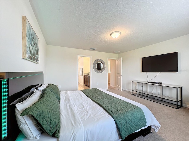 bedroom with ensuite bath, a textured ceiling, and carpet flooring