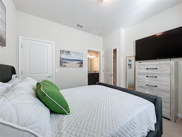 bedroom with a textured ceiling, ensuite bath, and light carpet