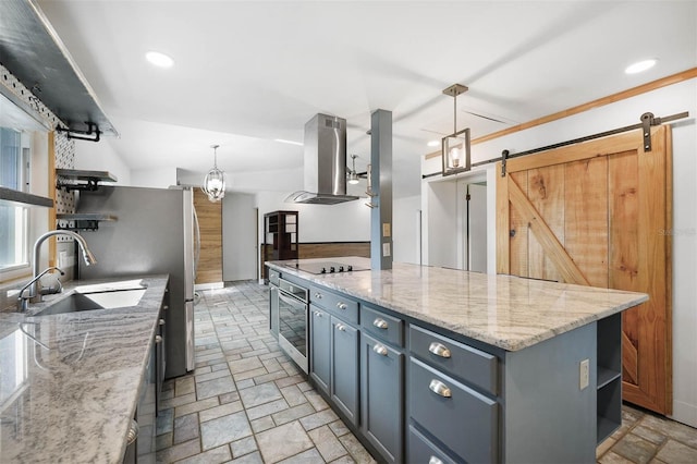 kitchen with hanging light fixtures, a barn door, range hood, a kitchen island, and light stone counters