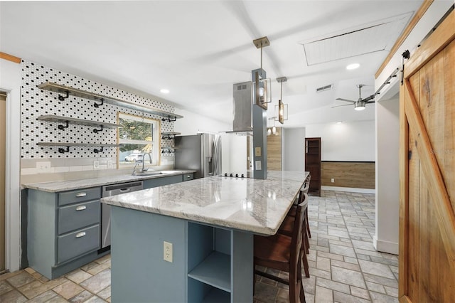 kitchen with sink, hanging light fixtures, a barn door, appliances with stainless steel finishes, and a kitchen island