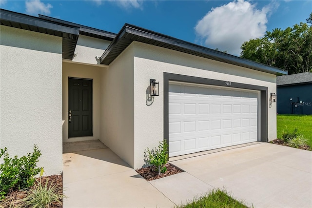 property entrance with stucco siding, an attached garage, and concrete driveway