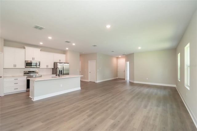 kitchen featuring backsplash, visible vents, light wood-style flooring, a kitchen island with sink, and appliances with stainless steel finishes