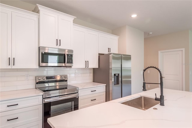 kitchen featuring light stone countertops, tasteful backsplash, appliances with stainless steel finishes, white cabinetry, and a sink