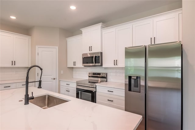 kitchen featuring white cabinetry, tasteful backsplash, stainless steel appliances, a sink, and light stone countertops