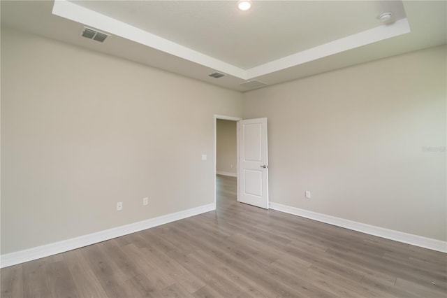 unfurnished room featuring baseboards, visible vents, wood finished floors, and a raised ceiling