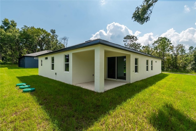back of property with stucco siding, a patio, and a yard