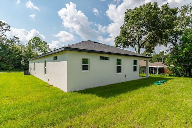 rear view of property featuring a lawn, a shingled roof, central AC unit, and stucco siding