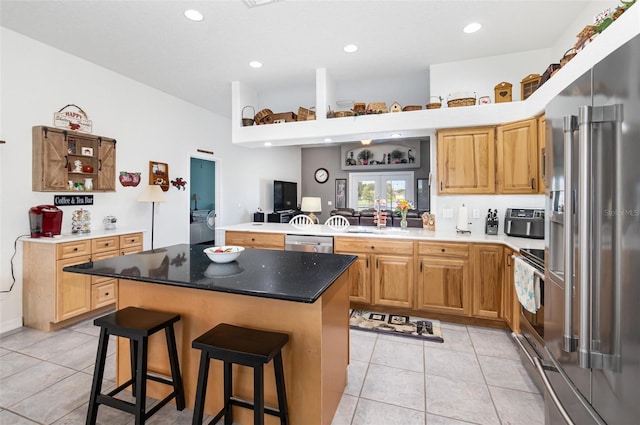 kitchen featuring light tile patterned floors, kitchen peninsula, a kitchen island, appliances with stainless steel finishes, and a breakfast bar area