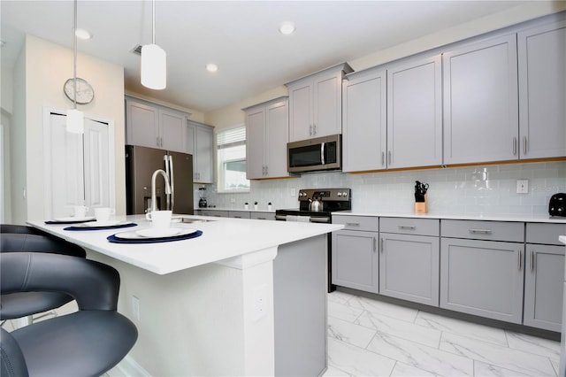 kitchen featuring appliances with stainless steel finishes, decorative backsplash, an island with sink, a breakfast bar area, and pendant lighting