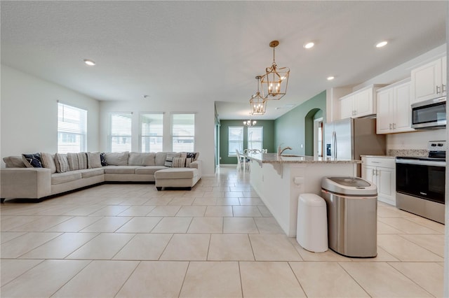 kitchen with appliances with stainless steel finishes, white cabinets, pendant lighting, a kitchen bar, and a kitchen island with sink