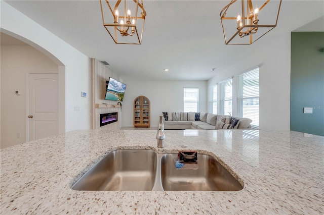 kitchen with hanging light fixtures, a fireplace, sink, and light stone counters