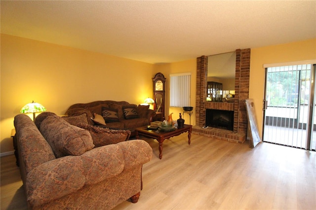 living room featuring a textured ceiling, light hardwood / wood-style floors, and a brick fireplace