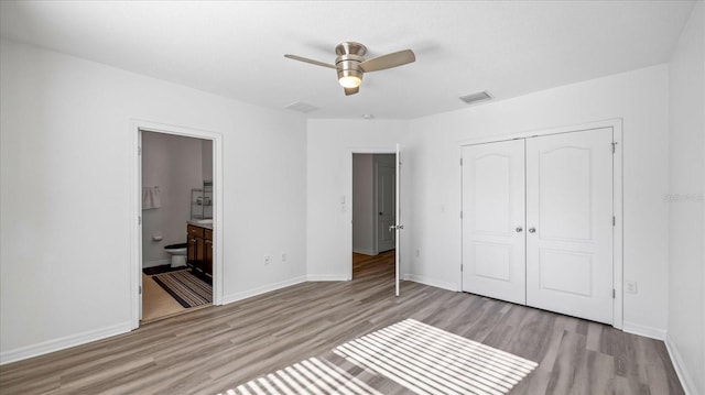 unfurnished bedroom featuring light wood-type flooring, a closet, ceiling fan, and ensuite bath