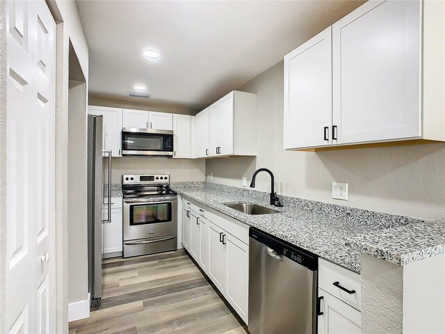 kitchen with sink, white cabinetry, appliances with stainless steel finishes, light stone countertops, and light hardwood / wood-style floors